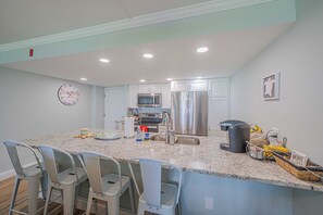 A kitchen with a central island, stainless steel appliances, and bar stools. - 1030 EastWinds S in Ponce Inlet, FL (Ponce Inlet)
