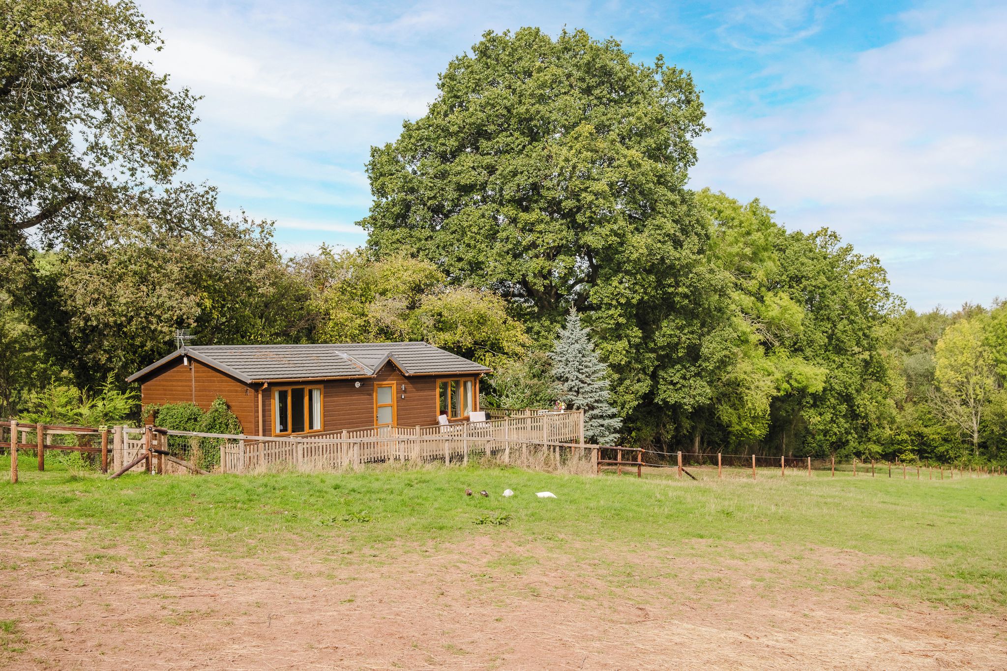 Eine Holzhütte mit umzäuntem Garten, umgeben von Bäumen.