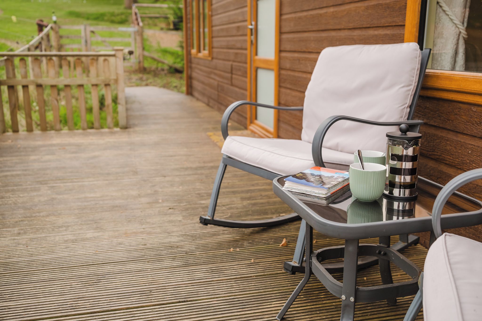 Eine Terrasse mit einem Metallstuhl und einem Tisch, einer Zeitschrift, einer Kaffeekanne und einer Tasse.