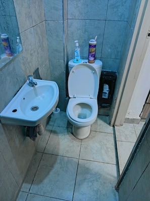 A bathroom with a white sink, toilet, and a shelf with toiletries. - Cozy Studio with Gym & Lift Prime location near TRM Mall (Nairobi)