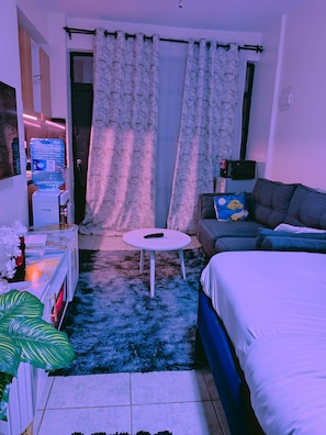 Ett modernt hotellrum med en säng, en soffa, ett litet runt bord, en vattenautomat och en tv.