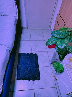 Een kamer met een bed, een blauw vloerkleed, een plant en een witte kast.