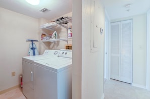 A laundry room with a front-loading washer and dryer, shelves above for storage, and a door leading to a closet. - Stunning Million Dollar Views- Seychelles 1106 (Daytona Beach Shores)