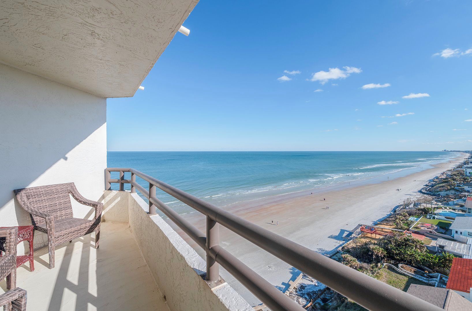 A balcony with a view of a beach and ocean, a chair, and a railing.