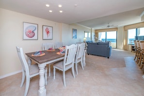 A dining area with a wooden table and white chairs, a sofa, and a view of the ocean. - Stunning Million Dollar Views- Seychelles 1106 (Daytona Beach Shores)