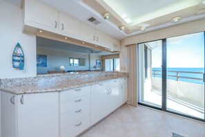 Eine Küche mit Granit-Arbeitsplatte, weißen Schränken und Meerblick durch eine Schiebetür.