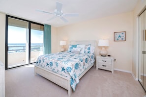 A bedroom with a bed, nightstands, a ceiling fan, a window with a view, and a framed picture on the wall. - Stunning Million Dollar Views- Seychelles 1106 (Daytona Beach Shores)