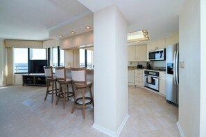 A modern kitchen with a central island, a dining area with bar stools, and a large window overlooking a scenic view. - Stunning Million Dollar Views- Seychelles 1106 (Daytona Beach Shores)