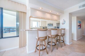 A modern kitchen with a central island, bar stools, and a large window offering a view. - Stunning Million Dollar Views- Seychelles 1106 (Daytona Beach Shores)