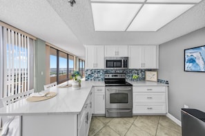 A modern kitchen with white cabinetry, a stainless steel stove, and a microwave. - 11D Royal Atlantic 2/2 ocean view unit (Daytona Beach Shores)