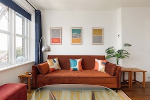 Ein modernes Wohnzimmer mit einem braunen Sofa, farbenfrohen Kissen, einem Glastisch und einem Blumentopf.