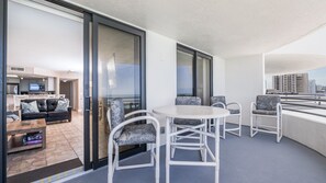 A modern apartment with a balcony, a dining area with white chairs, a sofa with patterned cushions, and a kitchen in the background. - 12th Floor Oceanfront 2/2 with Exceptional Views at 1202 Sand Dollar (Daytona Beach Shores)