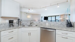 A modern kitchen with a granite countertop, stainless steel sink, and white cabinetry. - 12th Floor Oceanfront 2/2 with Exceptional Views at 1202 Sand Dollar (Daytona Beach Shores)