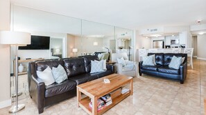 A modern living room with two leather sofas, a wooden coffee table, and a TV mounted on the wall. - 12th Floor Oceanfront 2/2 with Exceptional Views at 1202 Sand Dollar (Daytona Beach Shores)