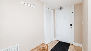 En gang med en hvid dør, knagerække og en lille træbænk.