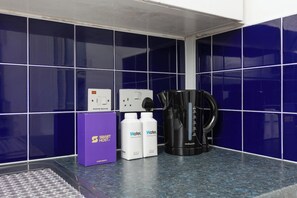 Eine Küchenzeile mit blauen Fliesen, einer Kaffeemaschine, zwei Wasserflaschen und einer violetten Schachtel mit dem Aufdruck 'SMART HOST'.