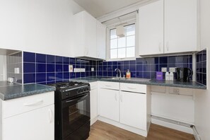A kitchen with white cabinets, blue tiles, a gas stove, and a coffee maker. - New! Bright Studio near Arsenal Station (Greater London)