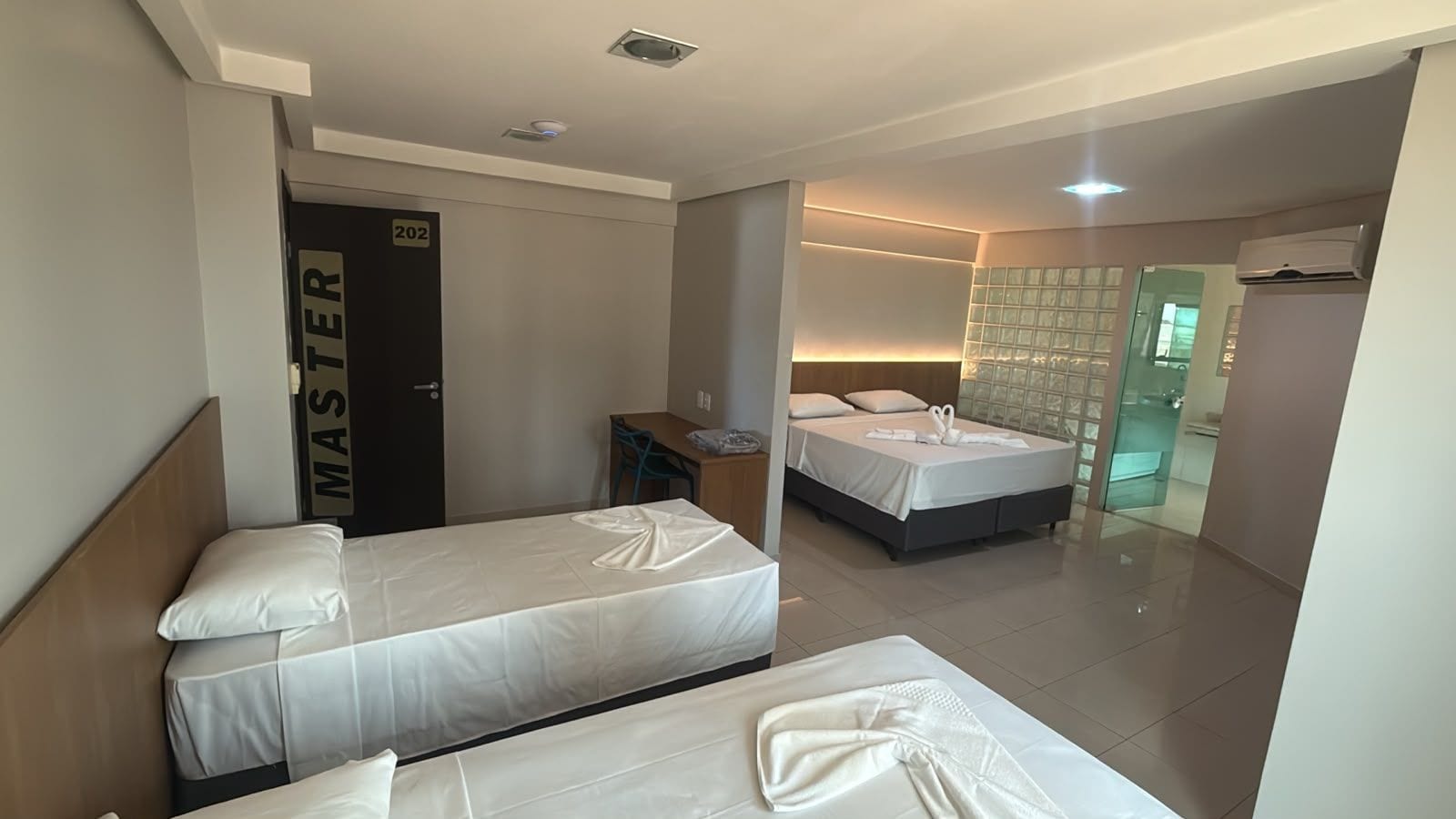 A hotel room with two beds, a desk, and a bathroom visible through a glass door.