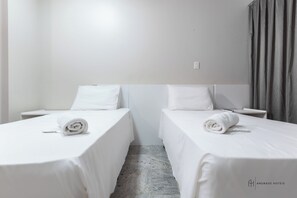A hotel room with two single beds, each with a neatly rolled white towel, a small bedside table, and a white wall. - Rede Andrade Munart (Palmas)