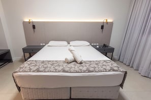Habitación de hotel con una cama grande, dos mesitas de noche, un televisor de pantalla plana y un teléfono.