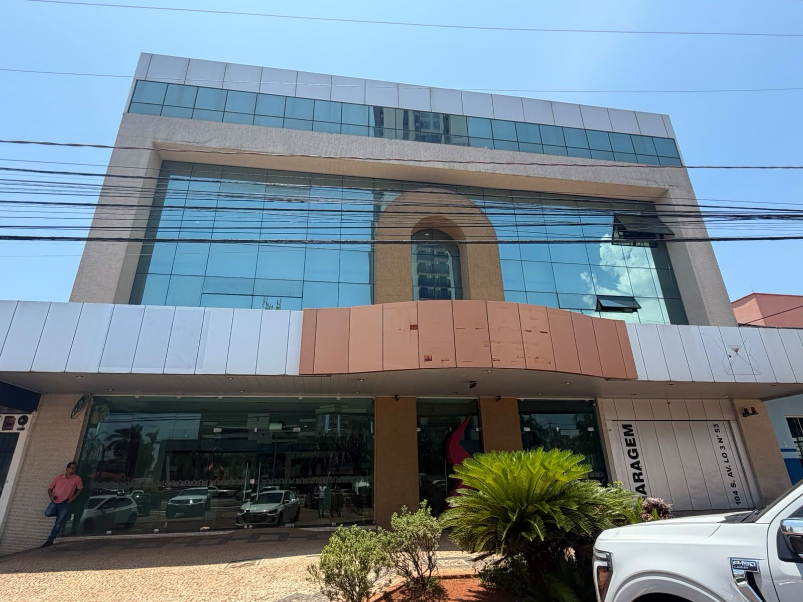 A modern building with a glass facade, a parking lot, and a sign that reads 'GARAGEM'.