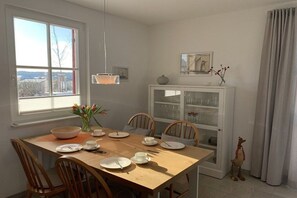 A dining area with a wooden table set for four, chairs, a vase with flowers, and a cabinet with glass doors. - Thatched house "Lütt Seeadler" (Zierow)