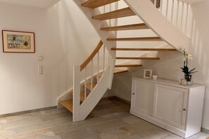 Eine Treppe mit Holzdielen und weißen Geländern, die zu einer Empfangsebene mit einem weißen Schrank und einem gerahmten Bild an der Wand führt.