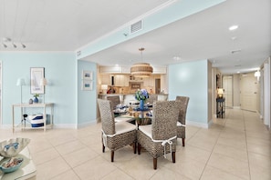 A dining area with a round table and four chairs, a kitchen in the background, and a hallway leading to a door. - #1404 Seychelles Oceanfront Traffic Free Beach (Daytona Beach Shores)