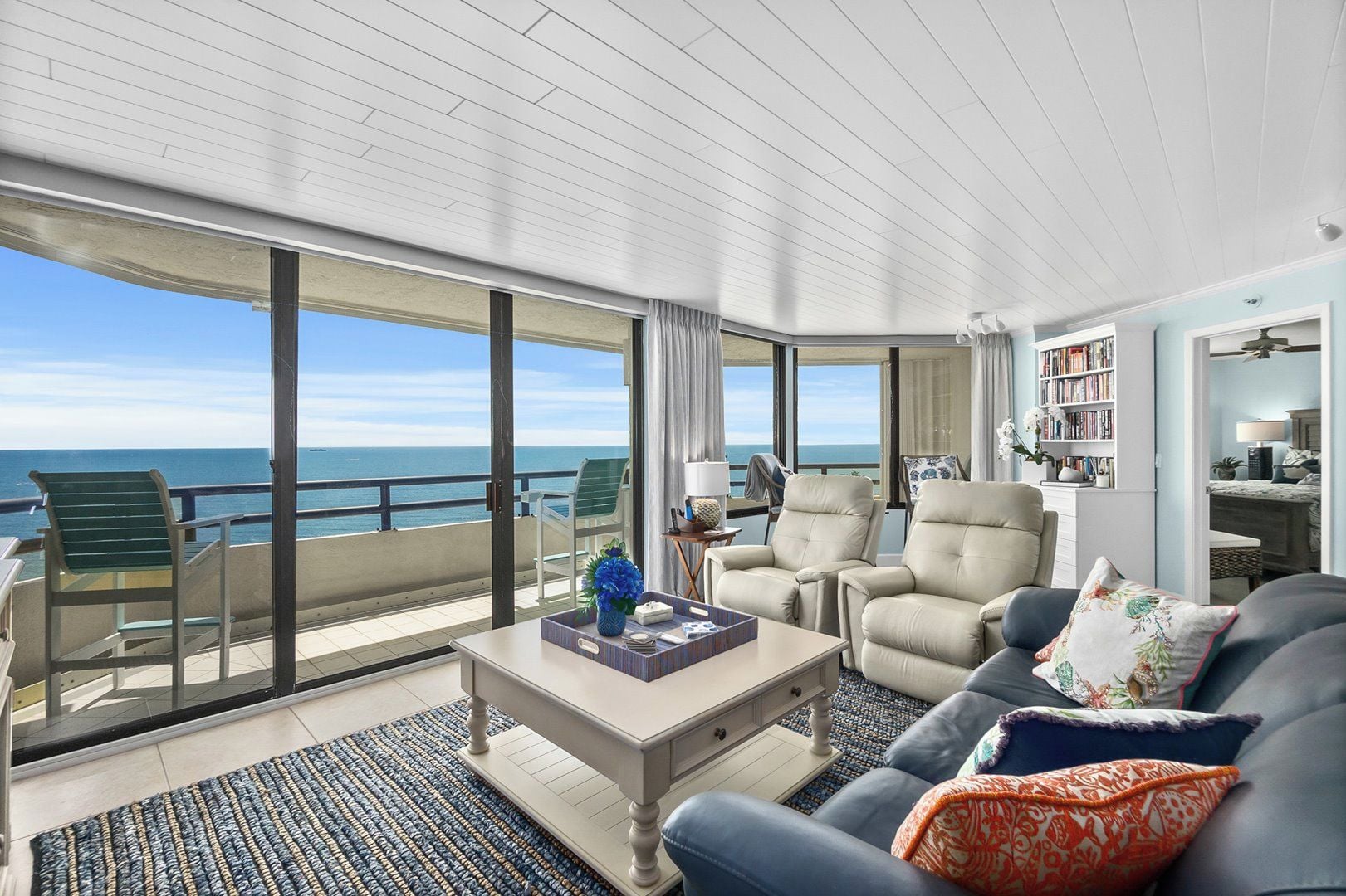 A spacious balcony with a view of the sea, furnished with a sofa, chairs, and a coffee table.