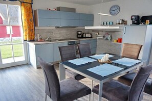 A modern kitchen with blue cabinets, a dining table with papers, and a clock on the wall. - Thatched house "Villa Selma" (Zierow)