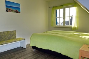 A bedroom with a bed, a bench, a window with curtains, and a picture on the wall. - Thatched house "Villa Selma" (Zierow)
