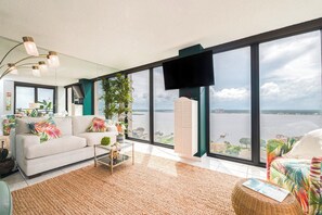 A spacious living room with a large window, a sofa, a coffee table, and a television. - 15B2 Oceans West in Daytona Beach Shores, FL (Daytona Beach Shores)