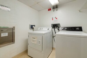 A laundry room with a metal trash can labeled 'Rubbish,' a washing machine, and a dryer. - 15B2 Oceans West in Daytona Beach Shores, FL (Daytona Beach Shores)
