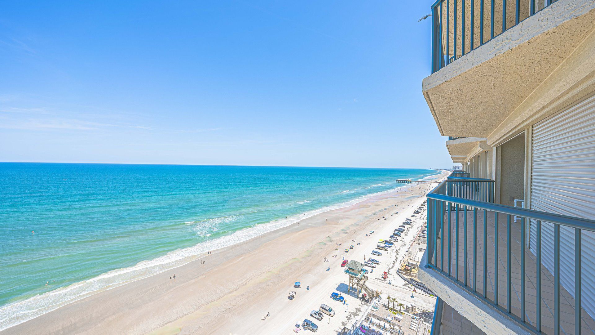 A beach view from a balcony with a clear sky, a sandy beach, and a calm sea.