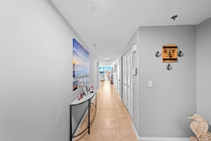 A hallway with a tiled floor, a table with framed photos, and a seahorse decoration on the wall. - 1B Royal Atlantic in Daytona Beach Shores, FL (Daytona Beach Shores)