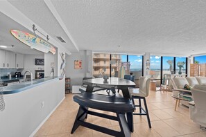 A modern kitchen with a bar area, a dining table, and a view of the city. - 1B Royal Atlantic in Daytona Beach Shores, FL (Daytona Beach Shores)