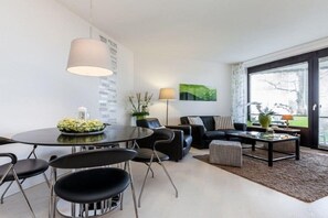 A modern living room with a round dining table, black chairs, a sofa, and a coffee table. - Holiday apartment with 1 bedroom (Travemünde)
