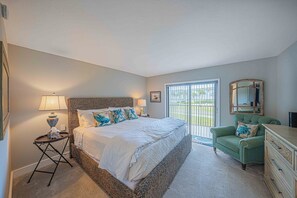 A bedroom with a large bed, a green armchair, a dresser, and a sliding glass door leading to a balcony. - 201 Tidewater in Ponce Inlet, FL (Ponce Inlet)
