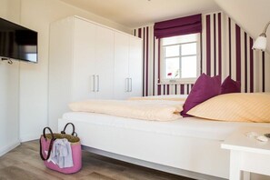 A bedroom with a bed, a TV mounted on the wall, a window with curtains, and a bedside table with a lamp. - Holiday home with 3 bedrooms (Fuhlendorf)