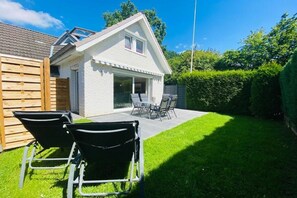 A house with a sloped roof, a visible window, and a patio area with a table and chairs. - Holiday home with 2 bedrooms (Sierksdorf)