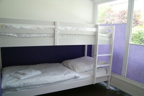 A bunk bed with white bedding and a window with blinds. - Holiday home with 2 bedrooms (Sierksdorf)