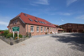 A brick building with a red-tiled roof, a gravel driveway, and a sign indicating a restaurant. - Holiday apartment with 1 bedroom (Fehmarn)