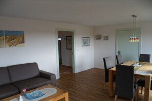 A living room with a sofa, a coffee table, and a dining area with chairs and a table. - Holiday home by the sea (Fehmarn)