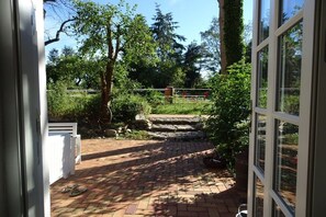 A patio area with a brick pathway leading to a white fence, surrounded by greenery and trees. - 4 holiday farm at Hemmelsdorfersee (Offendorf)