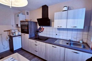 A compact kitchen with a built-in oven, a microwave, a black range hood, and a stainless steel sink. - "Holiday apartment at Kirr" (Zingst)