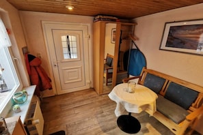Ein Zimmer mit Holzboden, einer weißen Tür mit Fenster, einem Tisch mit weißem Tuch, einem blauen Stuhl und einer Couch mit Kissen.