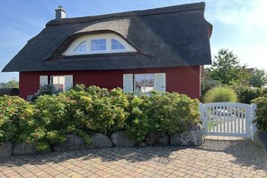 Ein rotes Haus mit einem Strohdach, einem weißen Tor und einem gepflegten Garten.
