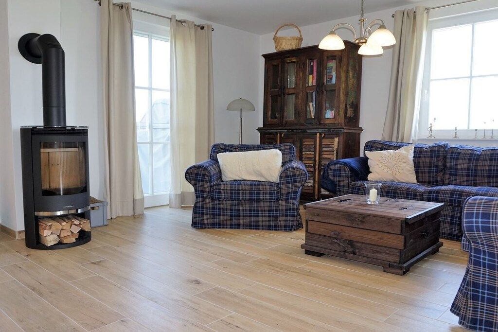 A living room with a wood-burning stove, plaid sofas, a wooden coffee table, and a cabinet with books.