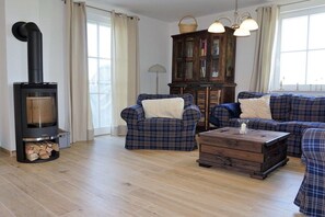 Ein Wohnzimmer mit Kaminofen, Karomüsseln, einem Holztisch und einer Bücherwand.