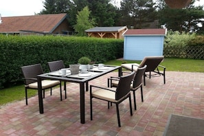 An outdoor patio with a table and chairs, a small shed, and a hedge in the background. - ||-----------------------Bodden Swallow------------------|| (Born am Darss)
